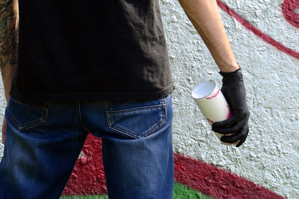 Unknown-figure-with-can-of-spray-paint-tags-wall-with-graffiti
